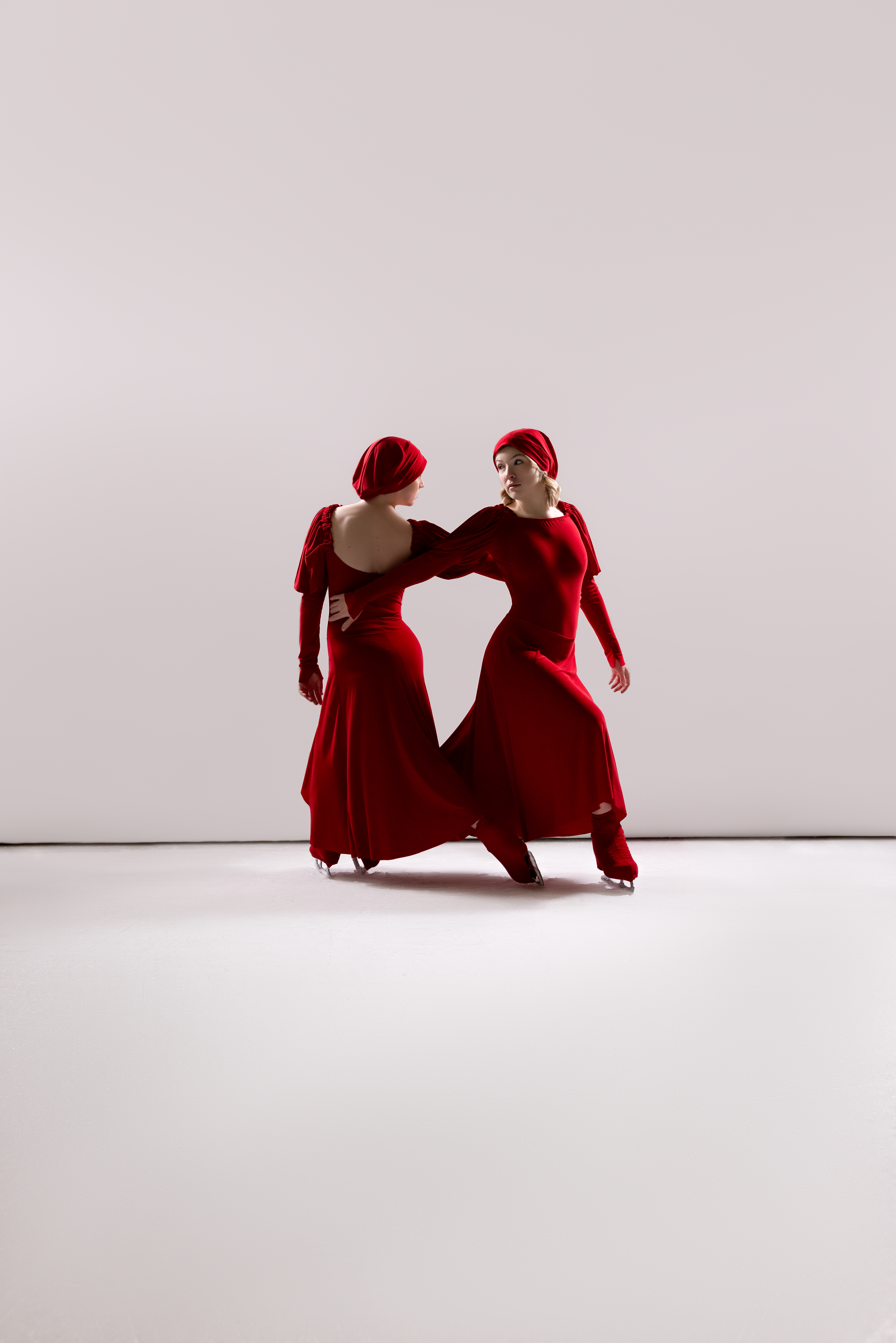 Two skaters in red, hands meeting at center